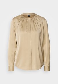 Blouse beige à manches longues avec encolure ronde et fronces discrètes autour du col, devant lisse avec patte de bouton cachée.