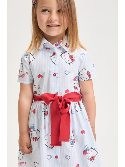 Νεαρή κοπέλα που φοράει ένα ανοιχτό μπλε φόρεμα με πρόσωπα Hello Kitty, κόκκινα καρδιές, κόκκινα κουμπιά και δεμένη κόκκινη υφασμάτινη ζώνη στη μέση.