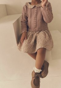 Pull en tricot rose avec un motif texturé et un col, associé à une jupe à imprimé floral. Chaussures marron et chaussettes blanches à volants.