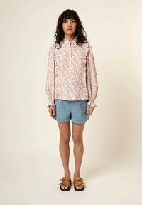 Blütenmuster langärmlige Bluse in Pastellfarben mit Rüschenmanschetten, kombiniert mit blauen, gestreiften Shorts und braunen Sandalen mit doppelter Schnalle.