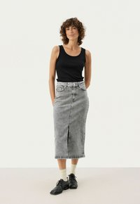 Sort ribbet tanktop parret med en højtaljet, knælang grå denimnederdel med en frontslids. Sorte sko og hvide sokker fuldender looket.