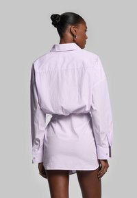 Robe chemise lilas rayée avec des manches longues, un col et des poignets boutonnés. Présente une taille cintrée et une coupe décontractée. Tissu en coton doux.