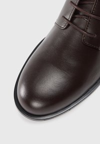 Zapato de vestir de cuero marrón con un acabado suave y pulido, punta redonda y suela delgada de goma negra. Presenta un diseño clásico de cordones.