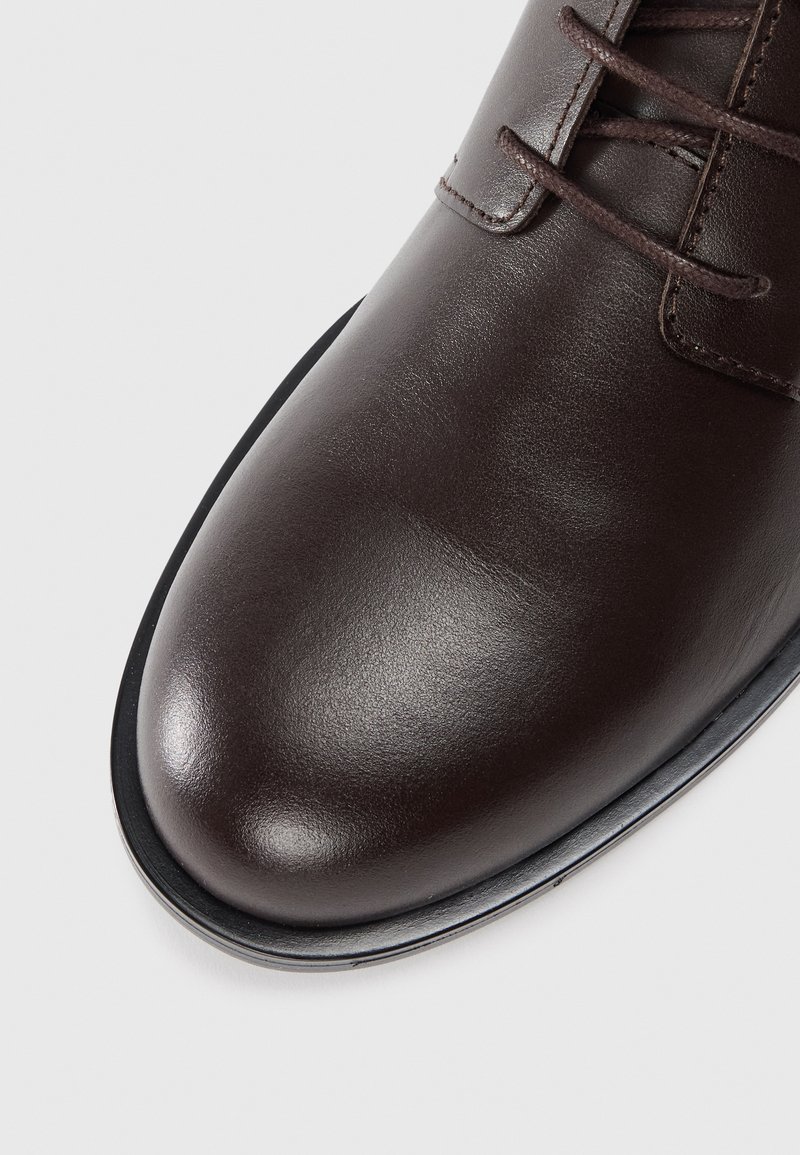 Chaussure habillée en cuir marron avec une finition lisse et poli, bout rond et fine semelle en caoutchouc noir. Présente un design classique à lacets.