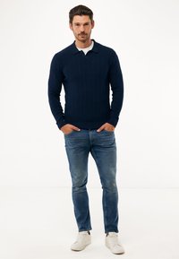 Námořnický proužkovaný polo s dlouhým rukávem, měkká pletená textura, v kombinaci s vybledlými modrými džíny a bílými teniskami, vytvářející neformální, vrstvený vzhled.