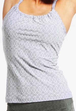 Femme portant un débardeur gris ajusté à motifs, sans manches, associé à un bas gris foncé sur fond blanc.