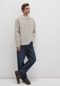 Gestreiftes Langarmhemd in Beige und Dunkelbraun, kombiniert mit lässigen blauen Jeans und braunen Wildlederschuhen. Einfaches, lässiges Design.
