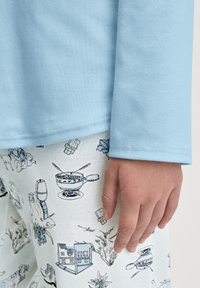 Maglietta blu a maniche lunghe con una texture liscia abbinata a pantaloni da pigiama bianchi con un motivo di disegni a linea nera di cibo e oggetti.