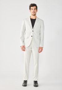 Lys grå pinstripe jakkesæt med en enkeltst�ående jakke med to knapper og slim-fit bukser. Båret med en sort t-shirt og sorte sko.