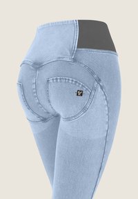 Vaaleansiniset farkut, joissa on kaareva ommel ja musta joustava vyötärönauha, nähtynä takaa lantion alueelta.