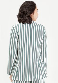 Blazer rayé vert et blanc, avec des rayures verticales, une coupe ajustée, des manches longues et une fente simple à l'arrière.