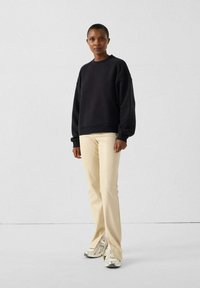 Felpa nera con vestibilità leggermente over-size, pantaloni beige aderenti e sneakers argento. Tessuto morbido, scollo tondo classico e maniche rilassate.