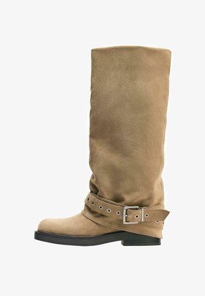 Beiger Wildleder-Stiefel bis zur Mitte der Wade mit flacher schwarzer Sohle und dekorativem Riemen mit Metallschnalle um den Knöchel.