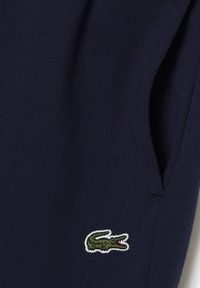 Marine bomullsstoff med en liten brodert grønn krokodillogo, glatt tekstur, og en tettsittende design med lommer.