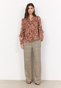 Blusa a maniche lunghe con un motivo a foglie rosse e beige, con spalle arricciate; abbinata a pantaloni a gamba larga a quadri e sandali aperti.