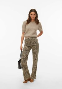 Pull beige à manches courtes en maille avec une finition texturée, associé à un pantalon large imprimé zèbre marron et vert. Sac à main noir.