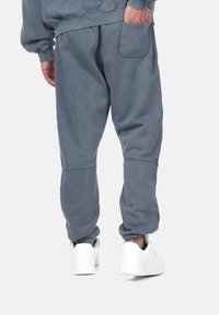 Un pantalon de jogging gris en tissu doux, avec une jambe fuselée, une poche latérale et des poignets élastiques, associé à des chaussures de sport blanches.