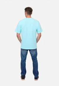 Camiseta de algodón de mangas cortas a rayas azul claro, llevada con jeans azul oscuro y zapatos negros, vista desde la parte de atrás.