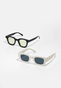 Două perechi de ochelari de soare: una neagră cu lentile verde deschis, formă rectangulară; una albă cu lentile gri închis, formă pătrată. Finisaj mat.