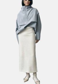 Grå, oversized pullover med høj krave og frontlynlås, parret med en kremfarvet, knælængde nederdel og mønstrede sokker.