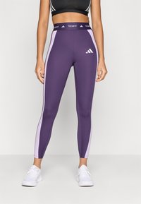 Leggings deportivos morados con paneles laterales rosas, cinturilla alta con "TECHFIT" y logo blanco de Adidas en la pierna izquierda.