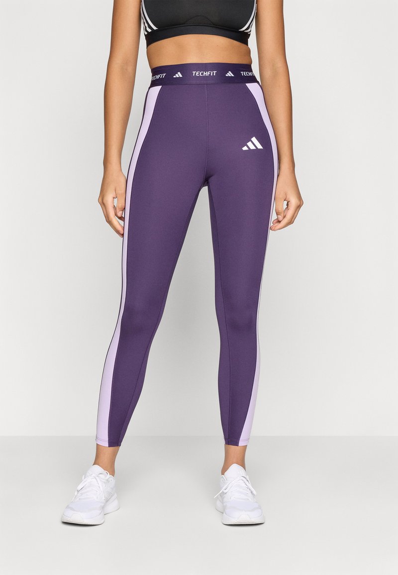 Leggings deportivos morados con paneles laterales rosas, cinturilla alta con "TECHFIT" y logo blanco de Adidas en la pierna izquierda.