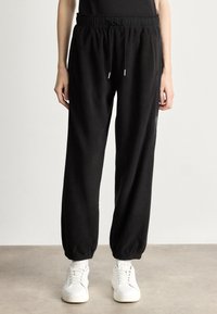 Czarne dresy z elastycznym paskiem i sznurkiem, z ribbowymi mankietami. W zestawie z białymi sneakersami.