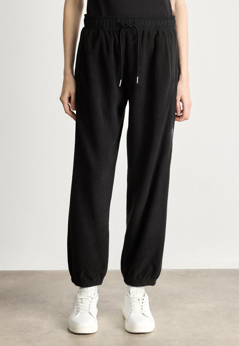 Czarne dresy z elastycznym paskiem i sznurkiem, z ribbowymi mankietami. W zestawie z białymi sneakersami.