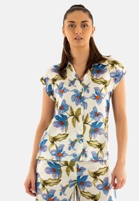 Camisa de manga corta de tela blanca con flores azules y centros naranjas, y hojas verdes. Diseño de botones y ajuste relajado.