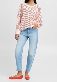 Un haut à manches longues rayé rouge et blanc associé à un jean bleu clair et des ballerines rouges. Le haut possède un col en V et une coupe décontractée.