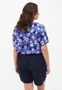 Top azul con estampado floral y mangas cortas, que presenta flores en azul, blanco y marino; combinado con pantalones cortos marinos, con cintura elástica.