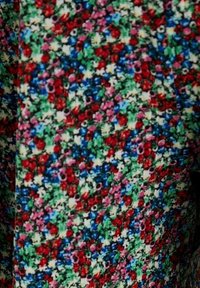 Motif de tissu dense avec de petites formes florales rouges, bleues, roses, blanches et vertes étroitement disposées sur toute la surface.