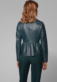 Teal leather jacket with a peplum waist and long sleeves, featuring a smooth texture and fitted design, viewed from the back.