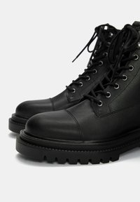 Stivali alla caviglia in pelle nera con punta rotonda, design con lacci, occhielli in metallo e suola in gomma robusta con un pronunciato motivo di battistrada.