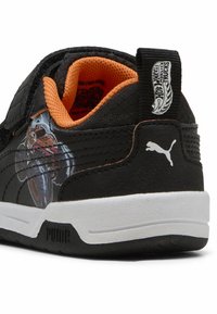 Crne i narančaste dječje tenisice s bijelim potplatima, s Puma logom i Hot Wheels Monster Trucks naljepnicom na tabanu pete.
