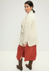 Creme katoenen shirtjack met voorzakken, gecombineerd met een roestkleurige midi-rok met een zijsplit en bruine cowboylaarzen.