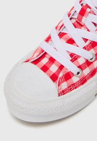 Rød og hvit rutete stoff sneaker med hvit gummitåhette og såle, med hvite snører og metalløyler for snøring.
