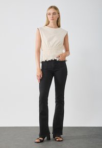 Haut sans manches beige clair avec une texture froncée à la taille et un volant noir. Associé à un jean noir évasé taille haute et des sandales à talons carrés.