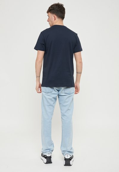 T-shirt marine à manches courtes, associé à un jean bleu clair. Modèle de dos, mettant en valeur un design simple et une coupe décontractée.