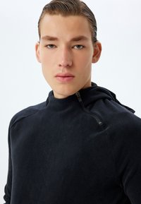 Svart fleece-pullover med dragkedja vid halsen, avslappnad passform och axelsömmar. Mjuk textur med en minimalistisk design.