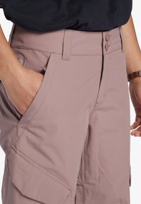 Helle rosa Cargo-Hosen mit zwei Fronttaschen, einem Reißverschluss und Druckknöpfen. Hergestellt aus glattem Stoff mit lockerer Passform.