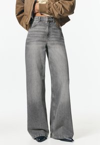 Jeans evazate, cu talie înaltă, din denim gri deschis. Prezintă o închidere standard cu buton și buzunare posterioare cu detalii de cusătură discreetă.