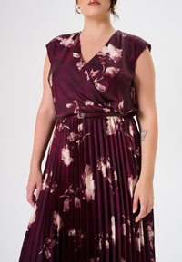 Pflaumenfarbiges Kleid mit kurzen Ärmeln, gewickeltem V-Ausschnitt, Blumenmuster und plissierter Rock. Inklusive einem schmalen Gürtel an der Taille.