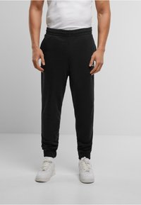 Zwarte sweatpants met een elastische tailleband, geribbelde boorden en een gladde textuur, gecombineerd met witte sneakers voor contrast.