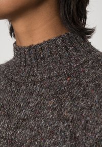 Maglione grigio a maglia con colletto alto a coste, superficie testurizzata con fletti multicolori e materiale morbido e caldo.