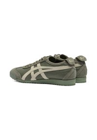 Green athletic shoes with a textured upper, featuring cream accents in a cross pattern, and a rubber sole. Laced closure with logo detail on heel.