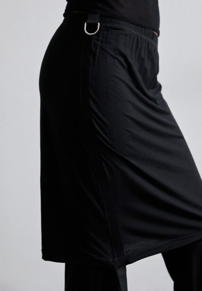 Saia atlética preta feita de material leve, com um cós elástico, uma fenda lateral e um detalhe em anel D de metal prateado.