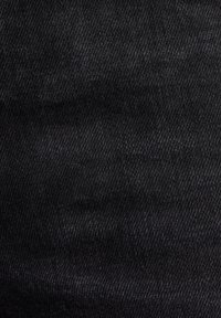 Gros plan sur un tissu en denim noir montrant une texture de tissage diagonal détaillée et des variations subtiles d’effilochage.
