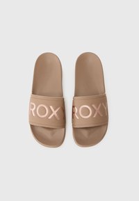 Brune sandaler med bred stropp som har rosa "ROXY"-bokstaver. Glatt syntetisk materiale, flat såle og rund tådesign.