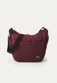 Burgundy fabric shoulder bag with a zippered closure, adjustable black strap, and logo patch. Soft, slightly padded material with a sleek design.
